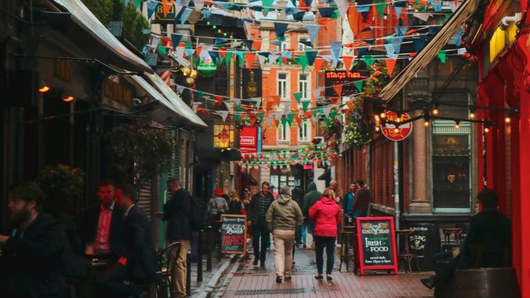 Rue animée avec des passants, guirlandes colorées et devantures de bars